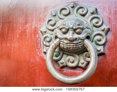 Bronze lion head door knocker in traditional Chinese design style. Weathered cracks in red wooden backing.