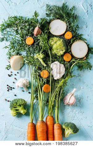 Raw vegetables for cooking soup. Ingredients young carrot with haulm, broccoli, cauliflower, onion, garlic, salt pepper over turquoise concrete background. Top view. Dinner cooking concept