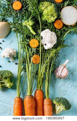 Raw vegetables for cooking soup. Ingredients young carrot with haulm, broccoli, cauliflower, onion, garlic, salt pepper over turquoise concrete background. Top view. Dinner cooking concept