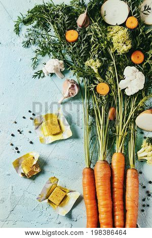 Raw vegetables and bouillon cubes for cooking soup. Young carrot with haulm, broccoli, cauliflower, onion, garlic, salt pepper over turquoise concrete background. Top view. Dinner cooking concept
