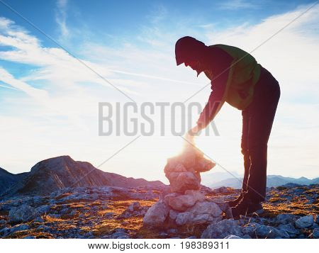 Alone Adult Man Is Stocking Stone To Pyramid.alps Mountain Summit, Evening Sun At Horizon.