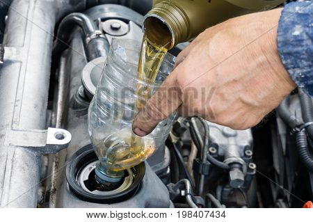 repairman is changing oil in car using old plastic bottle as a funnel