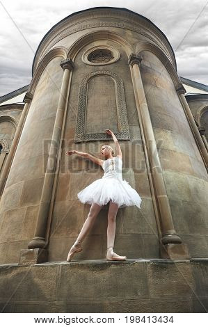 Young female ballet dancer in white outfit performing near epic old castle outdoors.