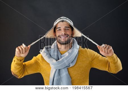 Portrait of smiling man holding wooly hat against black background