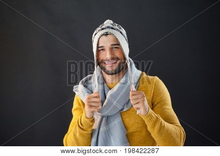 Portrait of smiling man holding wooly hat against black background