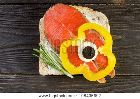 Delicious homemade smoked salmon canapes with cream garnished with a fresh rosemary leaf on dark wooden background. Seafood eating concept.