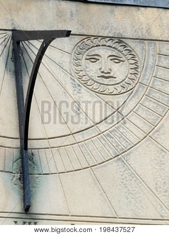 old sundial in close up with roman numeral and a carved symbol of the sun