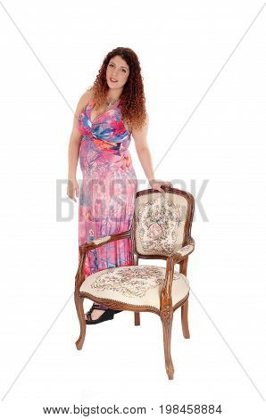 A beautiful Caucasian woman in a long colorful dress stranding beside an old fashion armchair isolated for white background