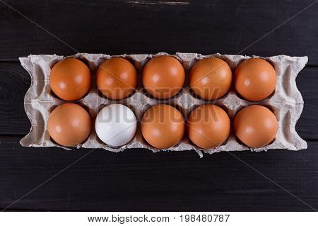 Container of ten eggs. Nine eggs brown one egg white. on black wooden background. Eggs container