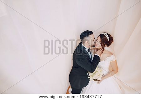 A beautiful young Turkish man wearing a black suit and a beard standing near tulle along with his beautiful bride in a white dress and a bouquet of flowers