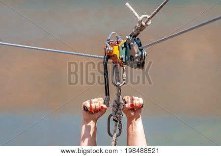 Zipline. Equipment for safe sliding on steel cable. Woman's hands close-up during the flight.