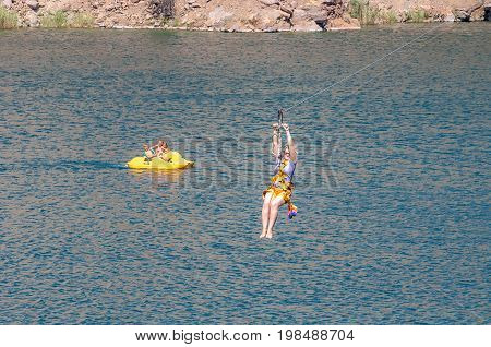 Zipline. The woman in the equipment slides on a steel cable. Trolley Track Over the lake. Extreme and active rest.