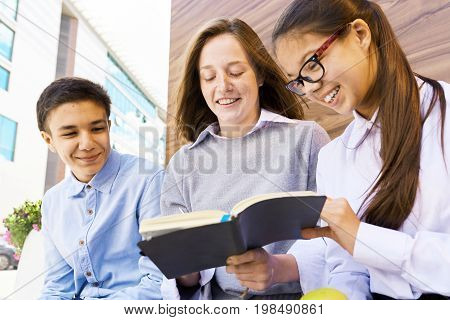 Portrait of three smiling school children reading book together outdoors