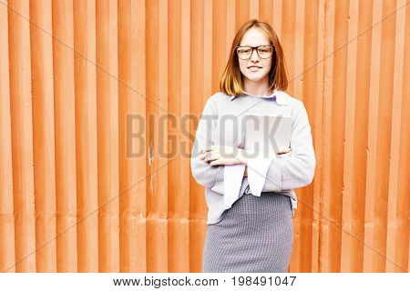 Portrait of smiling teenage school girl with red hair and freckles standing against orange wall
