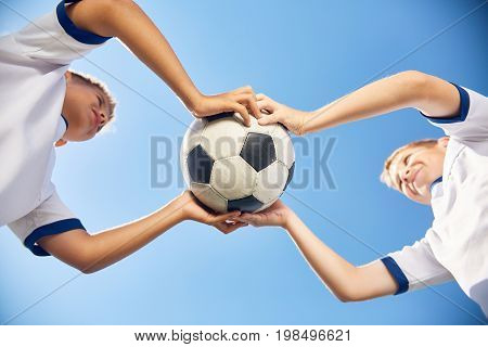 Low angle portrait of two boys in junior football team holding ball against clear blue sky