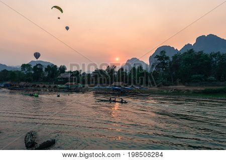 Wide angle picture of sunset over Nam Song River with hot air ballon and tourists on the boat in Vang Vieng Laos.