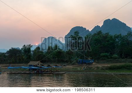The sun going down behind the mountains. Nam Song River with local vegetation in Vang Vieng Laos.