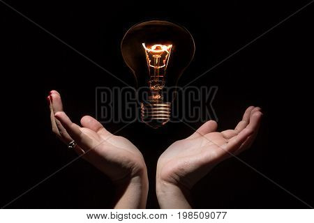 Idea and success coincept. Glowing light bulb without wires and opened female hands on black background
