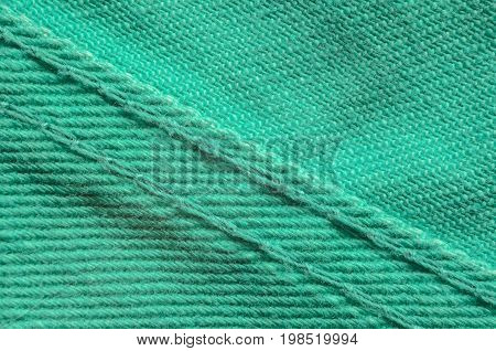 Green Denim Tissue Structure Textile Texture Close-up. Macro shot of the finishing seam on a green jeans product.