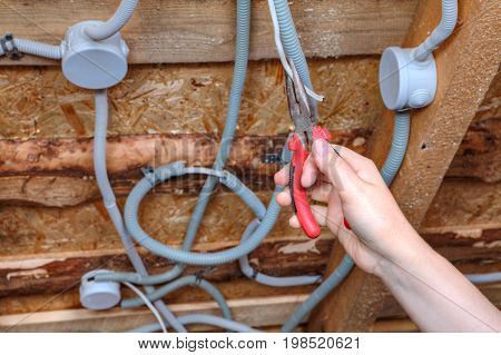 An electrician hand with pliers during installation mount light junction box wiring for ceiling.