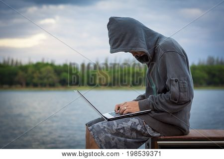 A Young Man Wearing A Hooded Sweatshirt Sitting Near The Old Television.a Hacker With A Laptop.