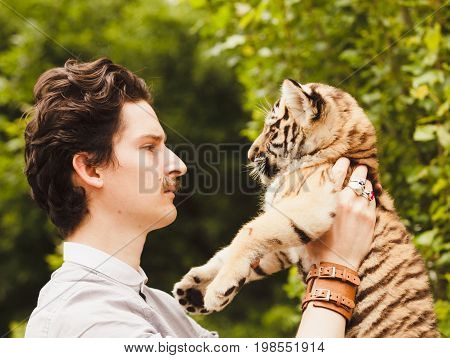 A man with a mustache looks into the face of a tiger cub otdoors
