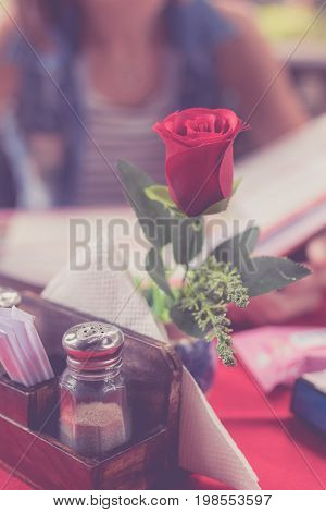 Close up of Rose in restaurant and woman with menu choosing dishes at restaurant on a blurred background. Bali island.