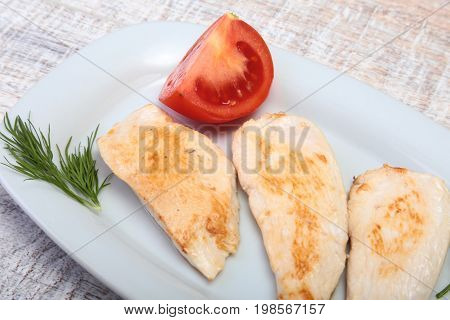 Slices of roasted chicken breast and tomato on white plate.