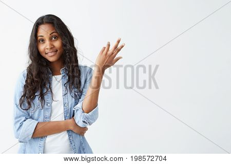Portrait of doubtful Afro-American young woman looking with puzzlement at camera isolated on white background. Pleasant-looking dark-skinned female dressed in denim shirt having confused and uncertain look