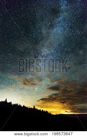 Milky Way And Sky Full Of Stars Reaching Across The Night Sky, Light From Horizon Behind Treed Mount