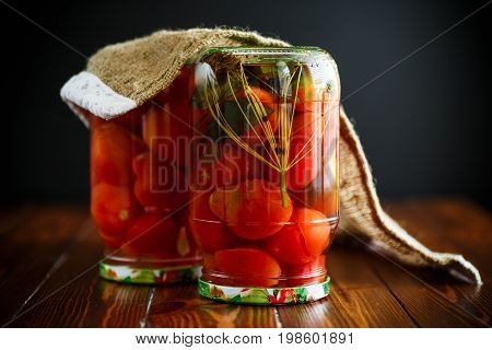 Home preservation. Canned in a glass jar ripe tomatoes on a wooden table.
