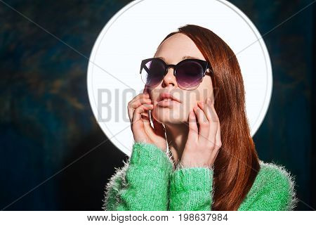 young redhead teen in greem pullover and sunglasses over dark blue background. beauty model woman with luxurious red hair. hairstyle.