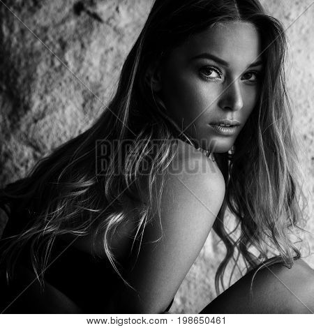 Fashion portrait of beautiful female model posing in black lingerie near white wall