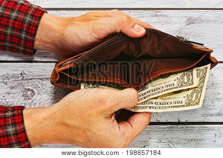 Man in checkered work shirt holding old leather wallet with just two US dollars - paying debt or poverty concept