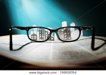 Eyeglasses lie on the open newspaper with paper houses. That could mean rent search purchase real estate. The template has lot of space for your text.