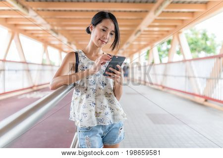 Woman looking at mobile phone in the foot bridge