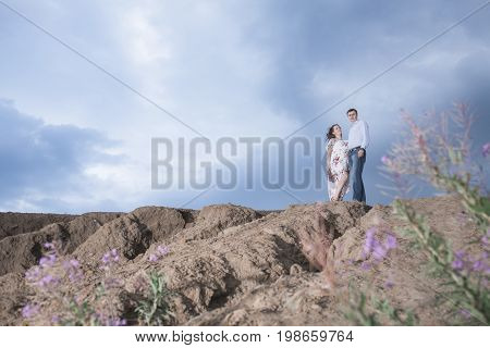 Happy pregnant couple in the mountains against the background of blue clouds