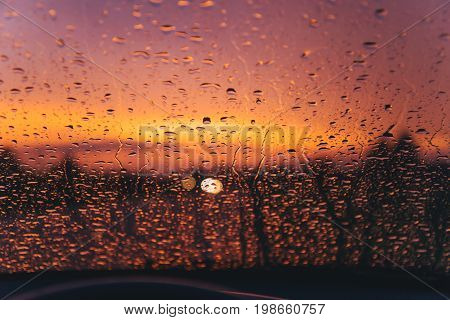 raindrops on car windshield on red sunset with bulred car lights on background