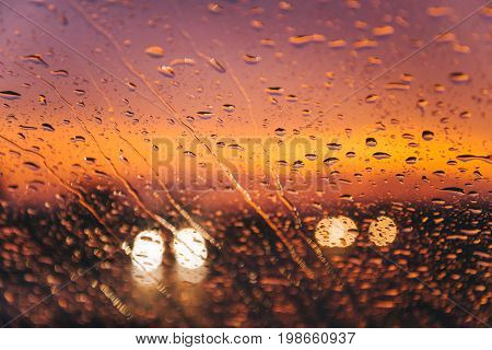 raindrops on car windshield on red sunset with bulred car lights on background