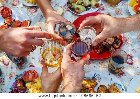 Hands of adult white people clink glasses with wine vodka and cola with ice over the table with homemade food.