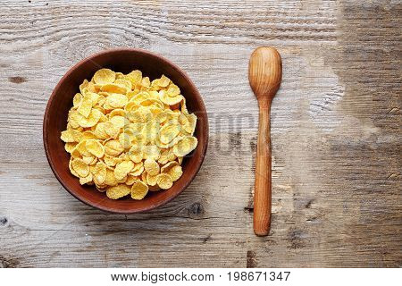 Corn flakes in a brown clay plate on a shabby wooden background next to a wooden spoon