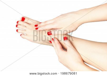 Woman with beautiful red manicured nails displaying her bare feet with her hands on her ankles on white. Fashion concept.