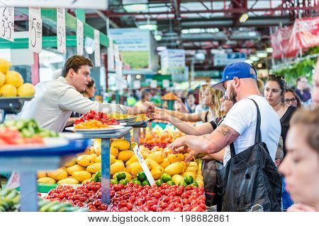 Montreal Canada - May 28 2017: People trying samples and buying produce by fruit and vegetable stands at Jean-Talon farmers market with coin change