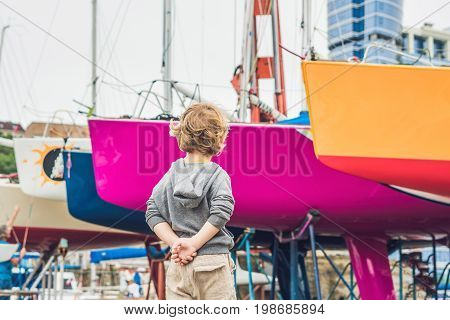 Cute Blond Boy Looking At Yachts And Sailboats