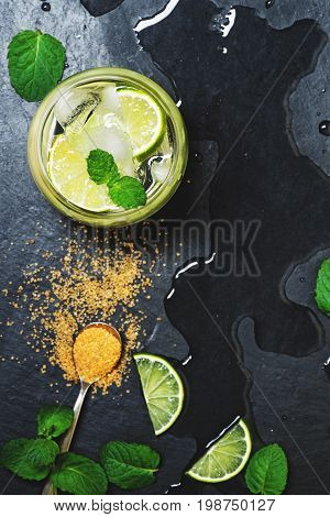 Refreshing mint cocktail mojito with rum and lime, cold drink or beverage with ice on black background, top view