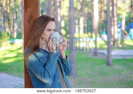Close up portrait of a smiling young girl in hat holding take away coffee cup outdoors