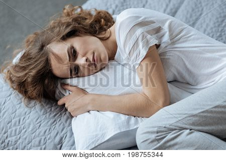 Bad day. Cheerless unhappy young woman resting on the pillow and thinking about her problems while having a bad day
