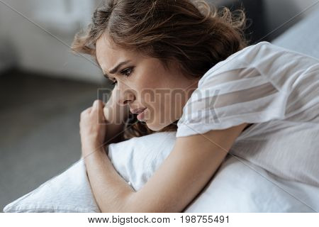 Personal problems. Cheerless sad young woman lying on the bed and feeling unhappy while having personal problems