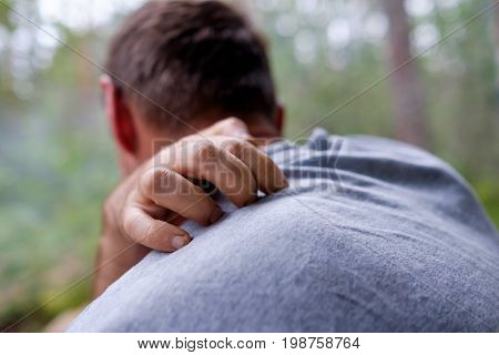 A person sits in the forest and scratches his back from pain or from insect bites. Unpleasant sensations.