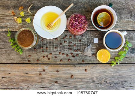 Tea, coffee in cups, chicory, lemon, mint, jam made of rose petals, dried lime, honey on the old wooden background. Toned image. Top view.
